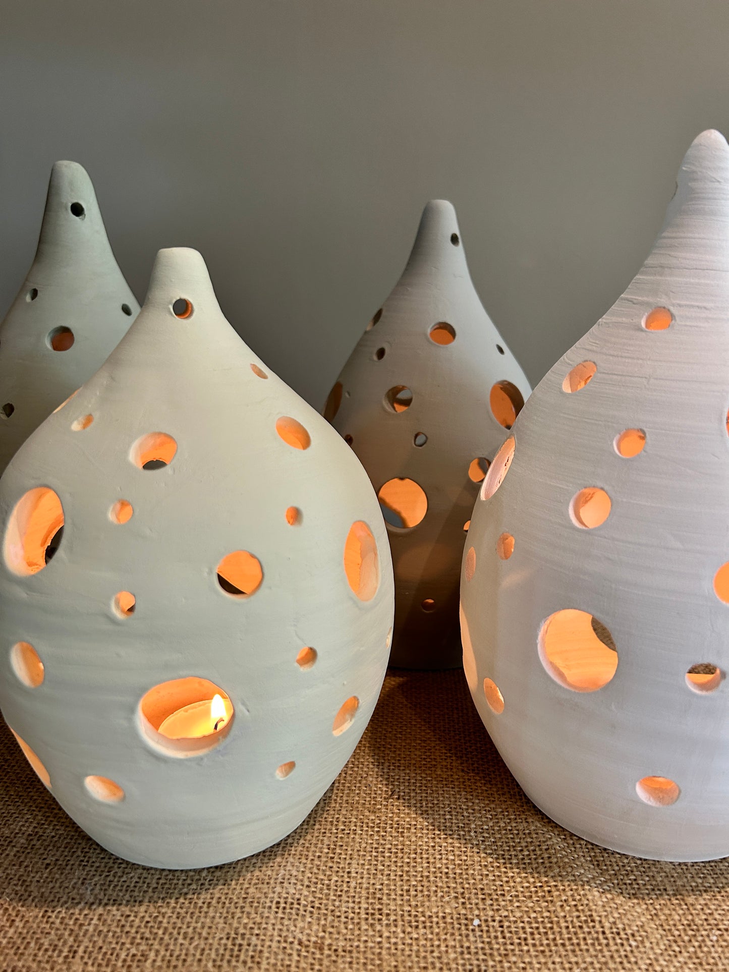 4 pottery lanterns with circles holes across them, lit from inside by candles 