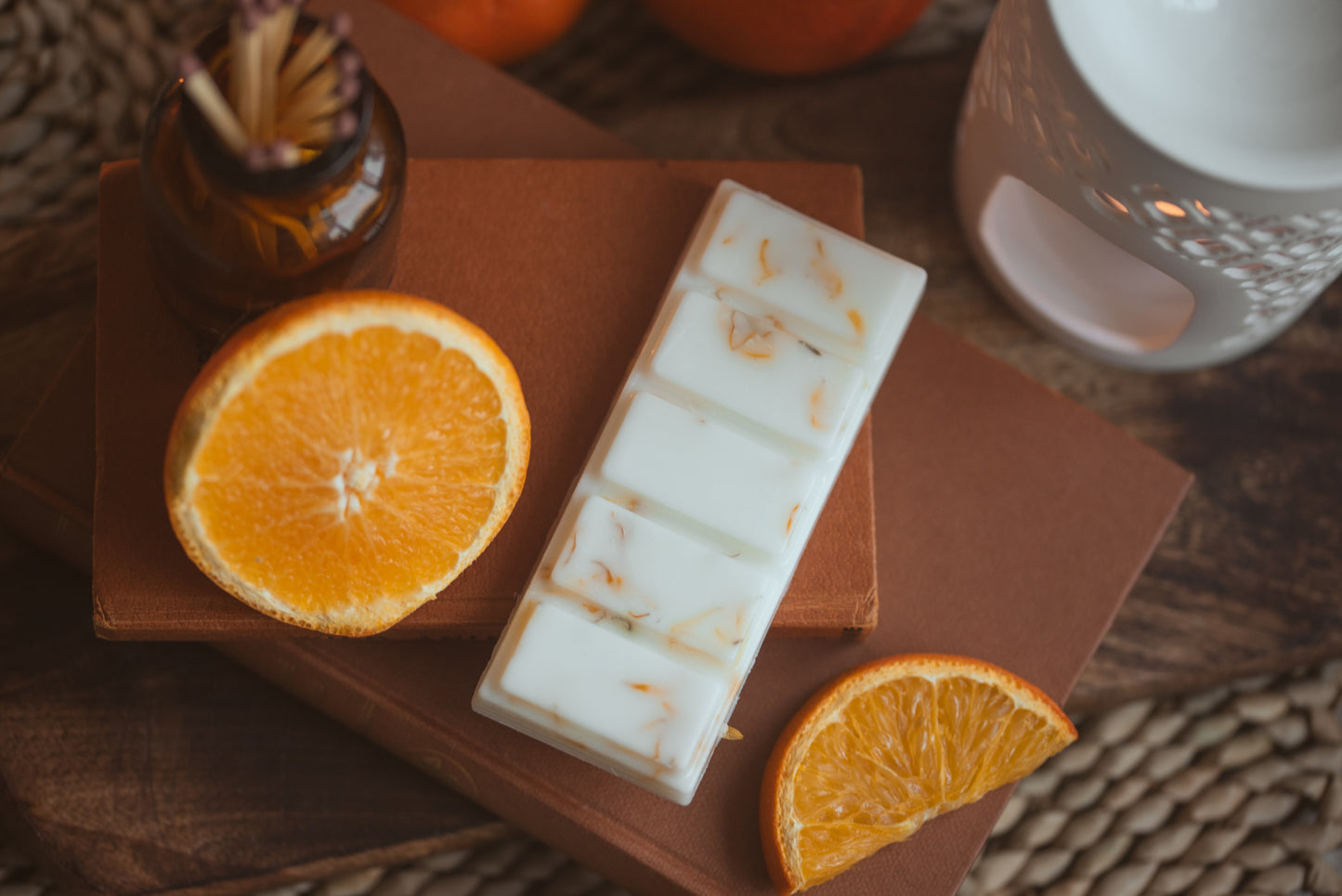 wax melt bar with 5 segments and sliced oranges, brown books and matches around the product 