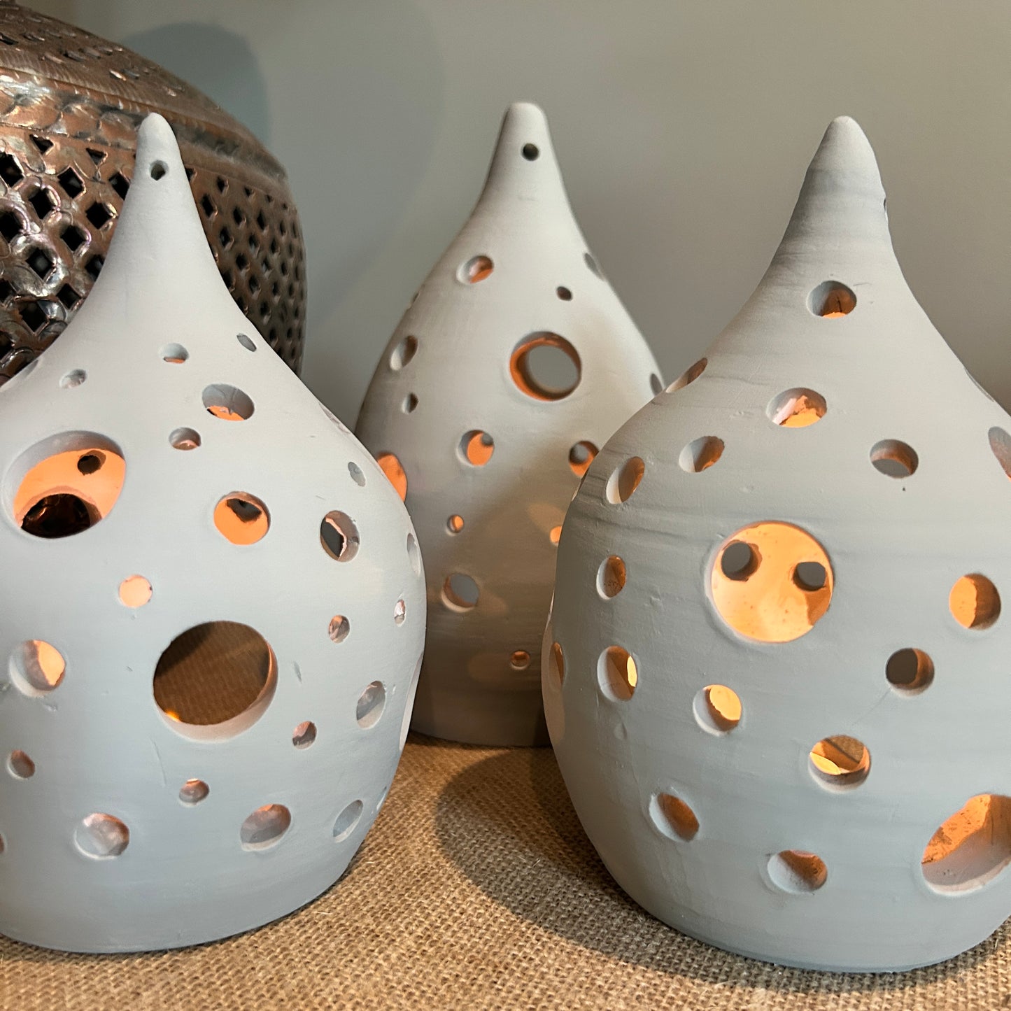 3 pottery lanterns with circles holes across them, lit from inside by candles 