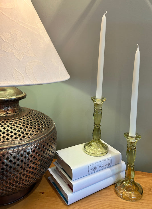 Two sage green candlesticks either tapered dinner candles with books and lamp beside 